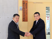 看板除幕式で手を取り合う山崎学長（左）と小河代表取締役社長（右）.JPG